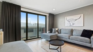 Un salon moderne avec un canapé gris, une table basse ronde et une grande fenêtre avec des rideaux.