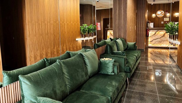 Een moderne receptie met een marmeren receptiebalie, groene banken en houten lambrisering.