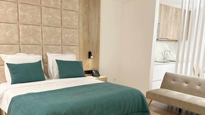 Een moderne hotelkamer met een groot bed, een nachtkastje met lamp, een sofa en uitzicht op de keuken.