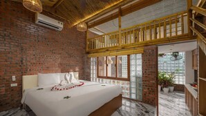 A hotel room with a brick wall, a bed with white linens, a wooden ceiling, and a view through a glass door. - Hoi An Golden Bamboo Villa & Spa (Da Nang)