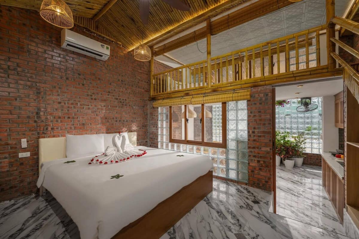 A hotel room with a brick wall, a bed with white linens, a wooden ceiling, and a view through a glass door.