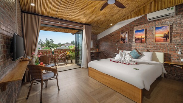 A modern hotel room with a large bed, a desk, and a balcony with a view. - Hoi An Golden Bamboo Villa & Spa (Da Nang)