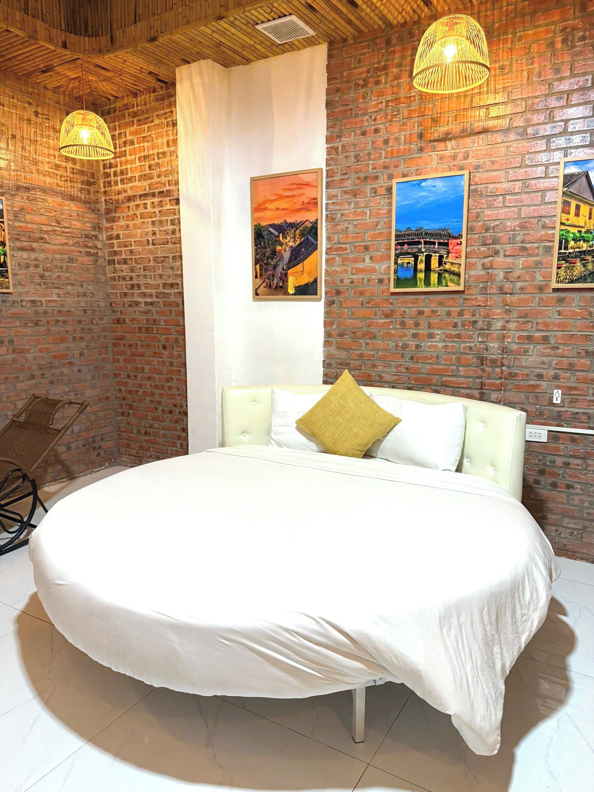 A large bed with a white bedspread, two pillows, and a headboard in a room with brick walls and a wooden ceiling.