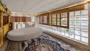 A bedroom with a large bed, a patterned rug, a brick wall, and a window with a view of greenery. - Hoi An Golden Bamboo Villa & Spa (Da Nang)