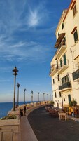 A seaside promenade with a row of buildings, outdoor seating, and street lamps.