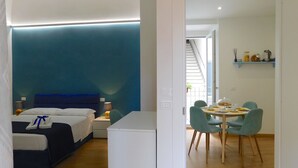 Une chambre d’hôtel moderne équipée d’un lit, d’une table de chevet, d’une lampe et d’un coin repas comprenant une table, des chaises et une machine à café.
