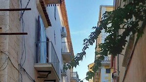 Une ruelle étroite pavée, bordée de bâtiments historiques dotés de balcons et de portes en arc de cercle.
