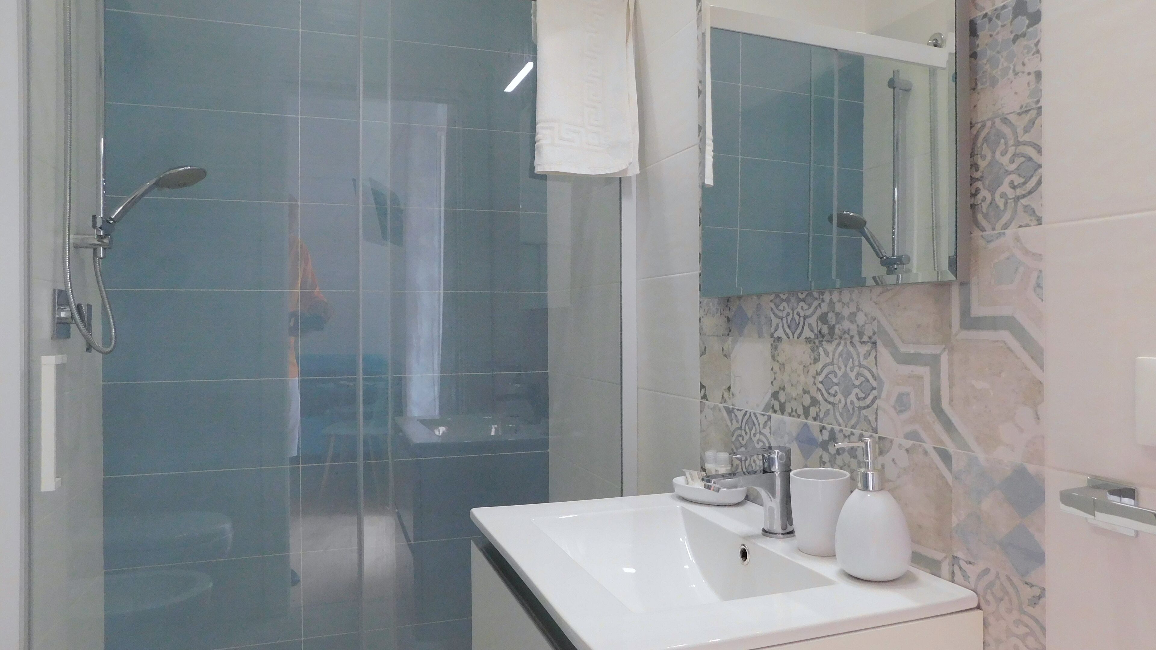 A modern bathroom with a glass-enclosed shower, a white sink with a mirror above it, and a patterned tile backsplash.