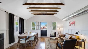 Uma sala de estar espaçosa com pé direito alto, vigas de madeira, área de jantar com mesa e cadeiras, sofá e luminária.