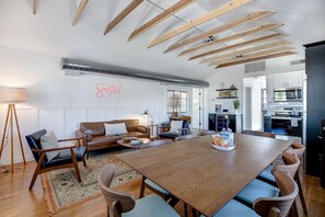 A spacious living room with a wooden dining table, a sofa, and a kitchen in the background.
