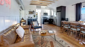 Sala de estar moderna com sofá, mesa de centro e área de jantar. Cozinha ao fundo, com eletrodomésticos e armários.