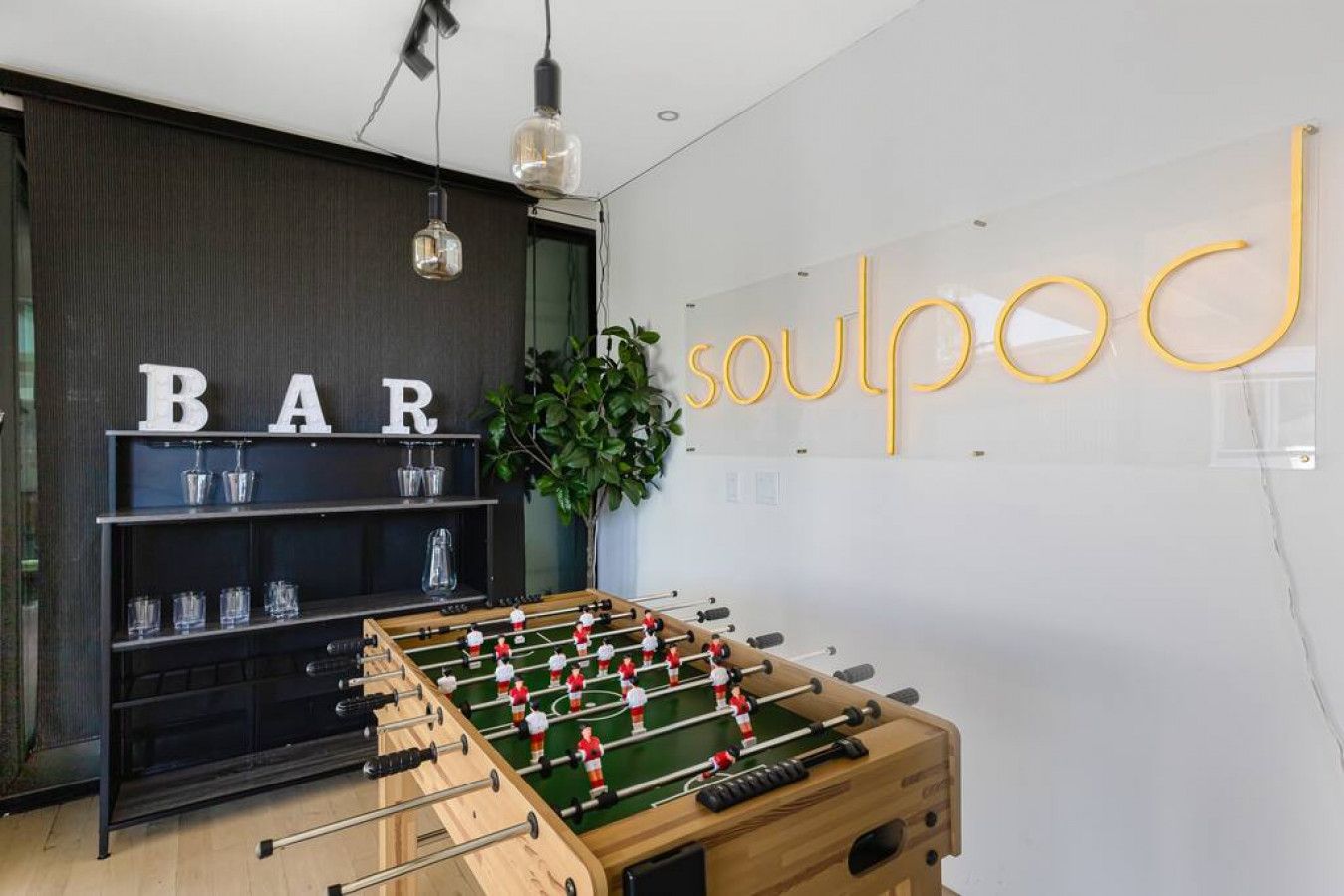 A room with a foosball table, a bar area with shelves, and a wall with the word 'soulpod' in yellow letters.