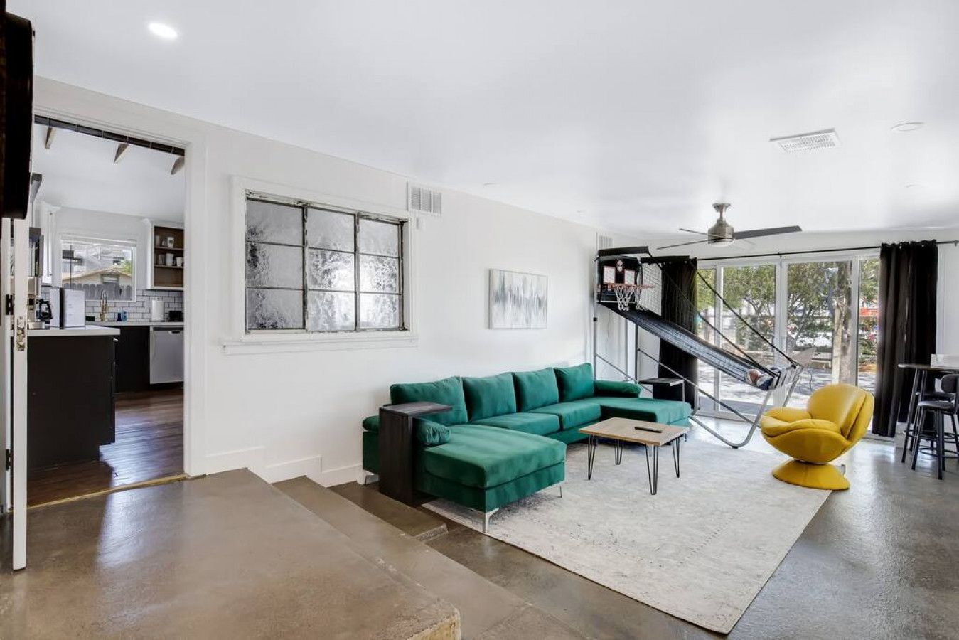 A modern living space with a green sectional sofa, a yellow chair, a staircase, and a kitchen area.