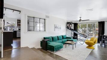A modern living space with a green sectional sofa, a yellow chair, a staircase, and a kitchen area.