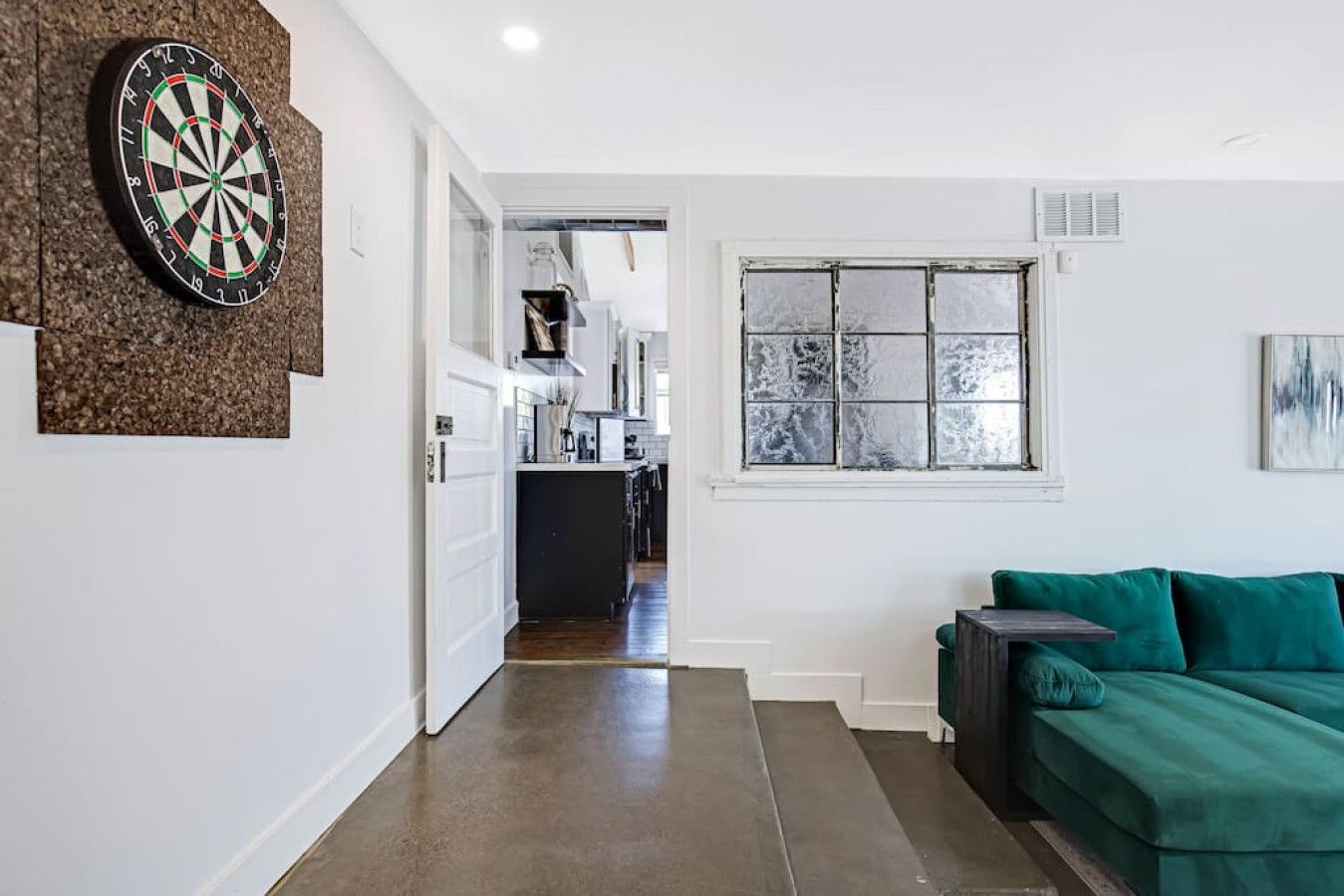 A hallway with a dartboard, a green sofa, and a window with frosted glass.