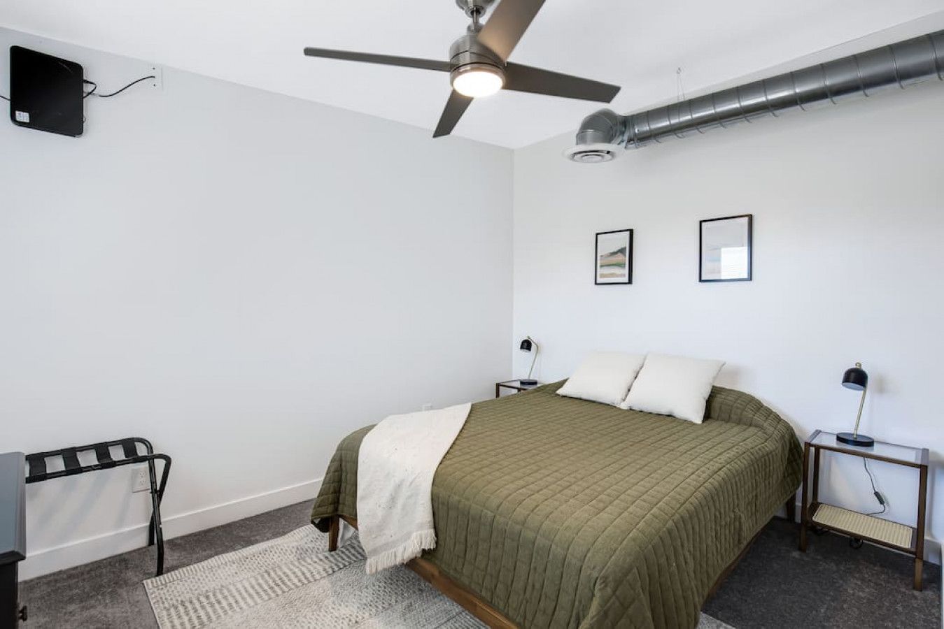 Een slaapkamer met een bed, een plafondventilator, een radiator en twee nachtkastjes met lampen.