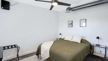 Een slaapkamer met een bed, een plafondventilator, een radiator en twee nachtkastjes met lampen.