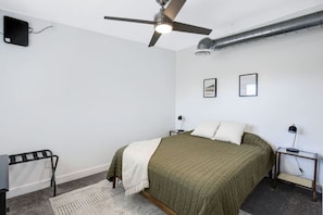 Een slaapkamer met een bed, een plafondventilator, een radiator en twee nachtkastjes met lampen.