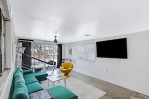 Een moderne woonkamer met een groene bank, een gele fauteuil en een flatscreen televisie aan de wand.