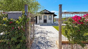 Uma casa com entrada por um caminho de paralelepípedos até a porta da frente, cercada por uma grade de metal e plantas floridas.
