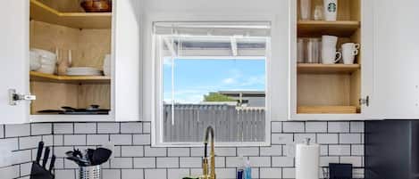 A kitchen with a double sink, wooden shelves, and a window with a view.