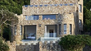 Un bâtiment en pierre qui ressemble à un château, doté d’un balcon et de grandes fenêtres, et entouré de verdure et d’une plage.