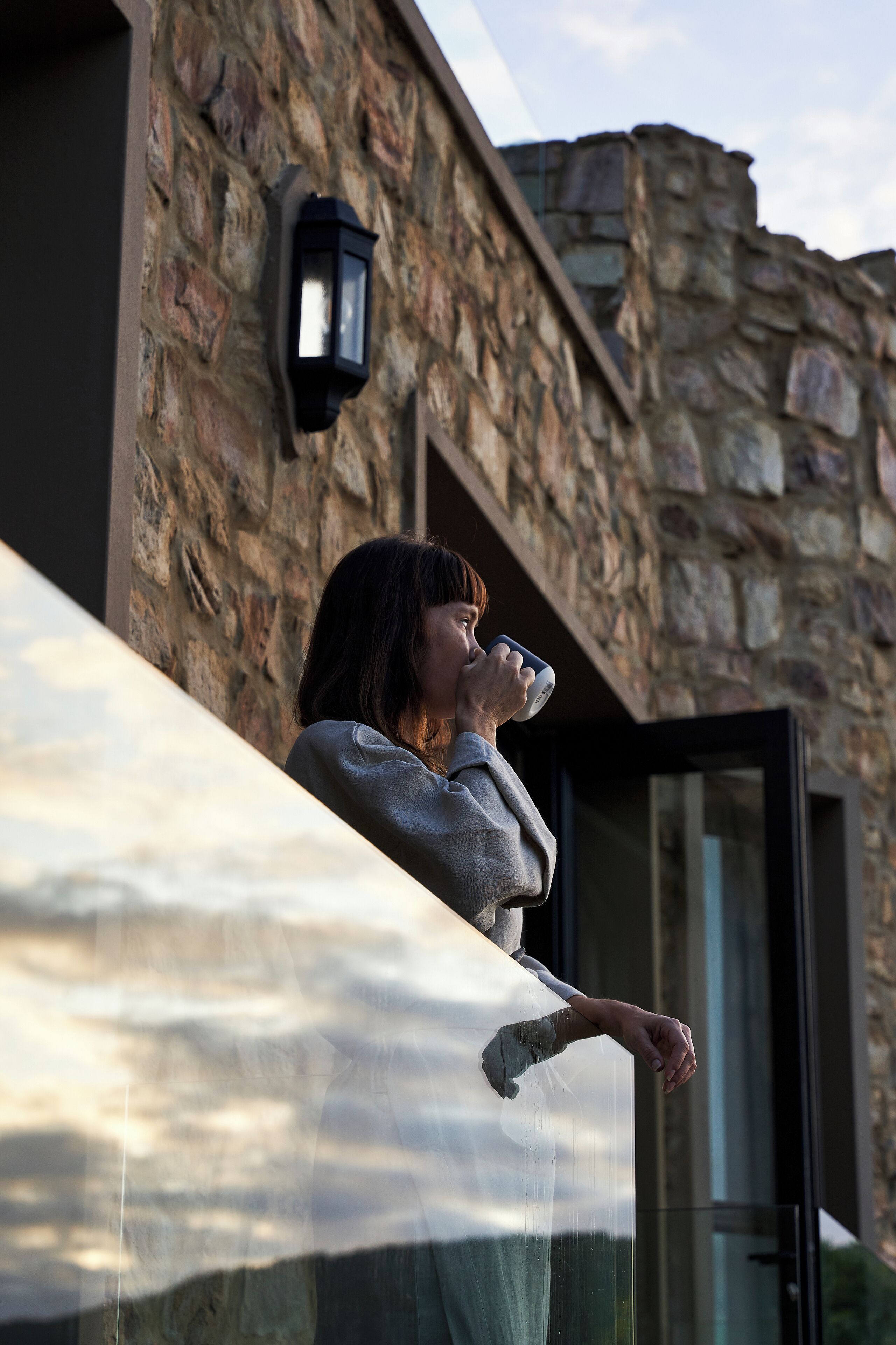 A person leaning on a glass door of a stone building with a stone wall and a lantern.
