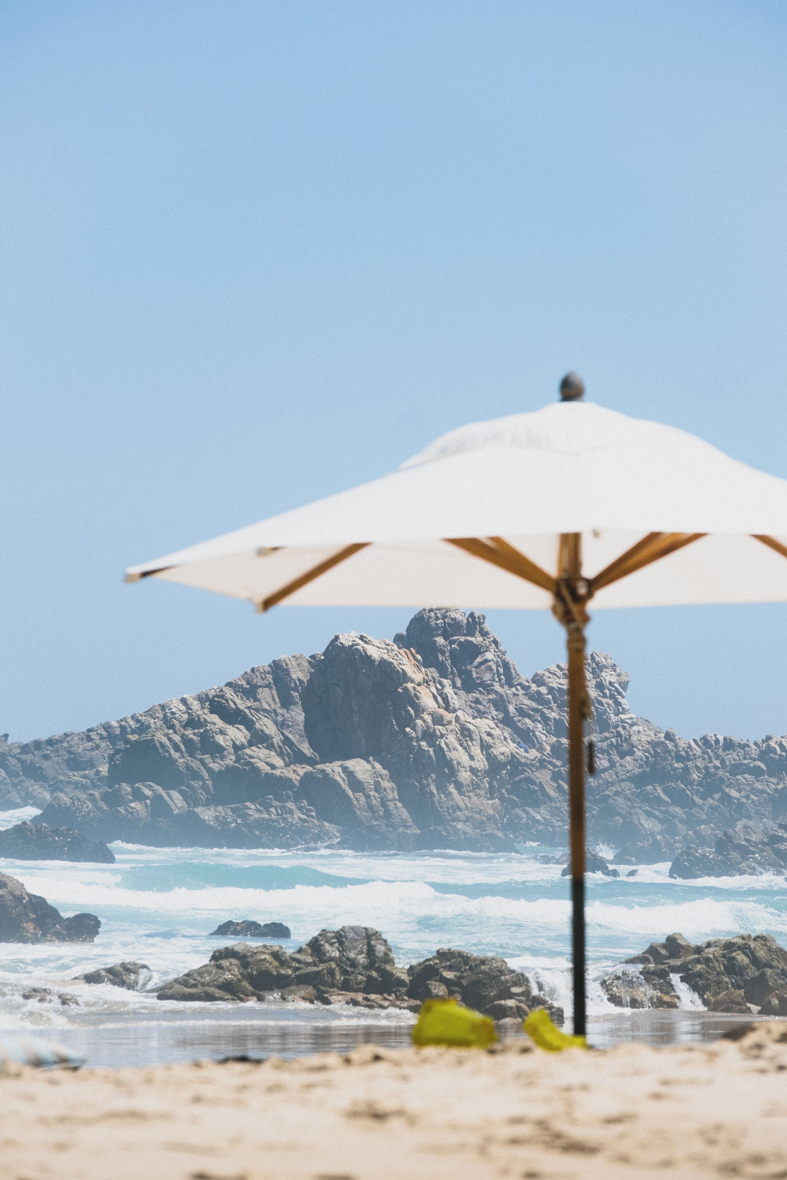 A beach with a white umbrella, rocky cliffs, and waves in the background.