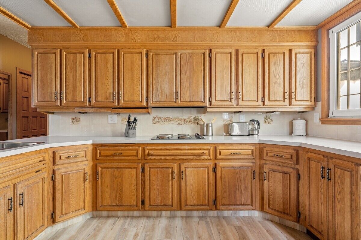 Keittiössä on puiset kaapit, valkoinen työtaso ja ikkuna oikealla puolella.
