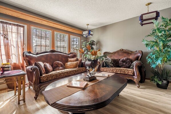 A living room with a dark brown leather sofa, a wooden coffee table, and a large window with curtains. - The Calgary Castle - Unique Stay (Calgary)