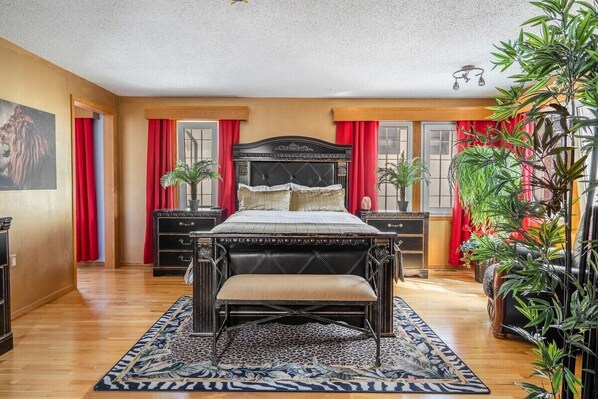A bedroom with a large bed, wooden flooring, red curtains, and a decorative rug. - The Calgary Castle - Unique Stay (Calgary)