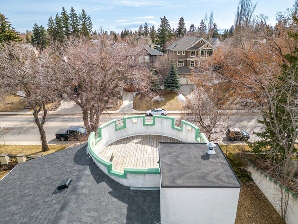 A circular outdoor deck with a wooden floor, surrounded by trees and a residential area in the background. - The Calgary Castle - Unique Stay (Calgary)