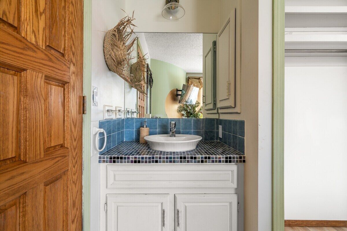 A bathroom with a white sink, blue mosaic tiles, and wooden cabinets.