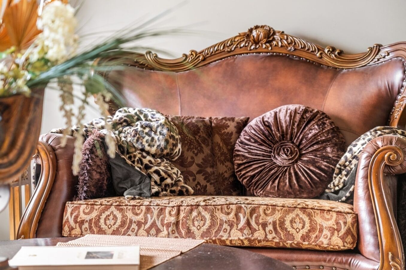 A brown leather sofa with ornate carvings, patterned cushions, and a decorative pillow.