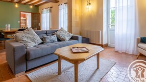 A cozy living room with a sofa, a wooden coffee table, and a dining area with a table and chairs. - Spacious Retreat: 5BR, Games Room, Forest Edge, and Large Garden Close to Château and Zoo (Baugé en Anjou)