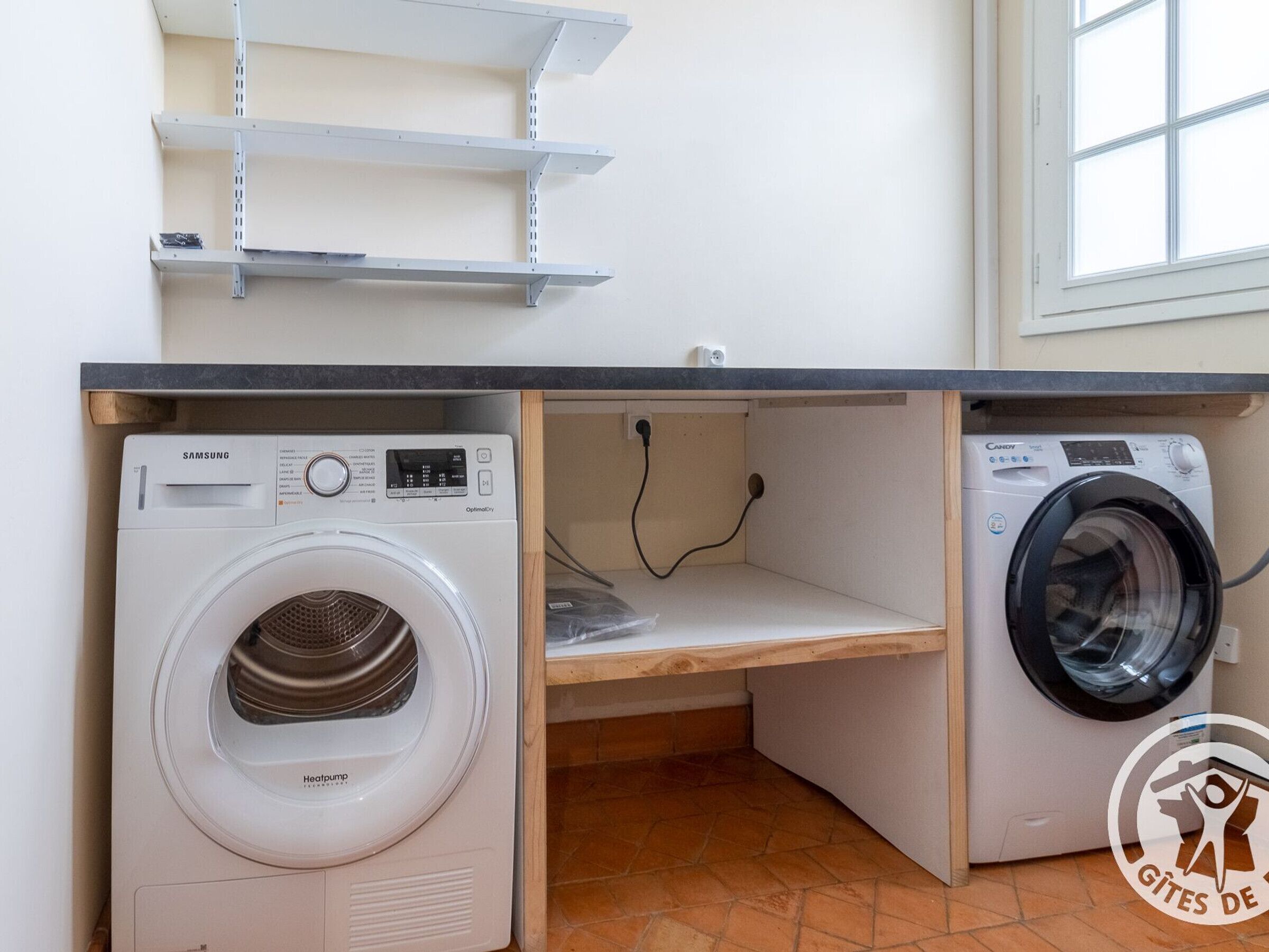 Een wasserij met een Samsung- en een Candy-wasmachine, houten planken en een betegelde vloer.