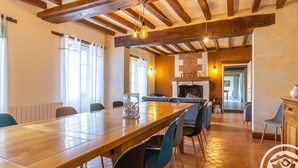A dining area with a long wooden table, blue chairs, a glass vase, and a brick fireplace. - Spacious Retreat: 5BR, Games Room, Forest Edge, and Large Garden Close to Château and Zoo (Baugé en Anjou)
