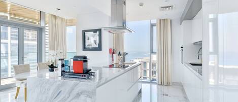 A modern kitchen with a marble island, stainless steel appliances, and large windows offering a view.
