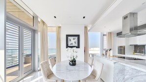 A modern kitchen with a marble countertop, a round dining table with chairs, and a view of the ocean through large windows. - Luxury 2BR plus maids room in Bluewaters (Dubai)