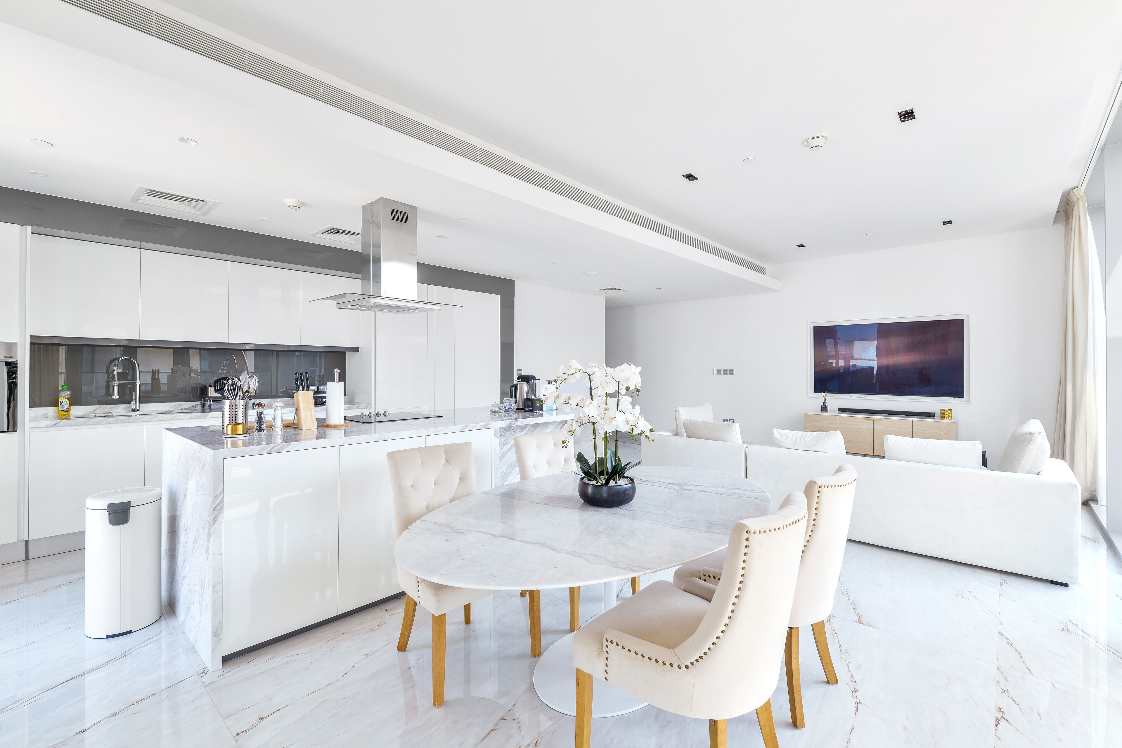 A modern kitchen with white cabinetry, a marble island, and a dining area with a round table and chairs.
