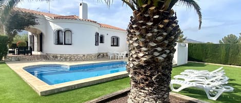 Una casa con piscina, una palmera y mobiliario de exterior.