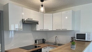 A compact kitchen with white cabinets, a black oven, a stainless steel sink, and a microwave.