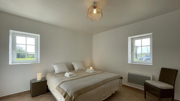 A bedroom with a large bed, two bedside tables, a chair, and a ceiling light fixture.