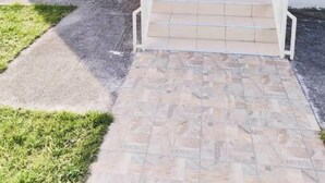 A building entrance with a white door, a small porch area, and a tiled pathway leading to the door. - Sweet Little Home Trikala (Pyli)