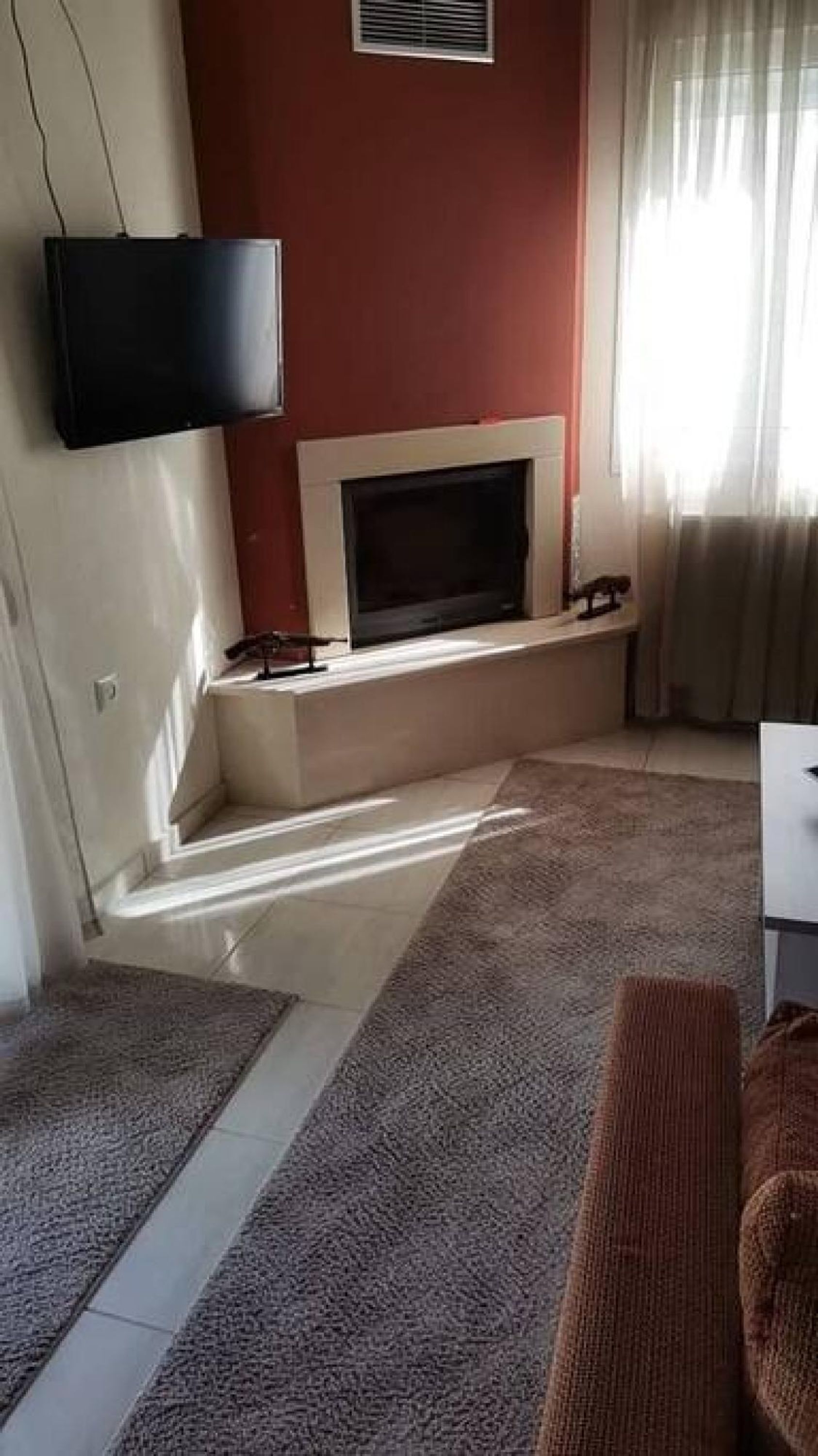 Un salon doté d’un téléviseur à écran plat fixé au mur, d’une cheminée et d’une grande fenêtre agrémentée de rideaux.