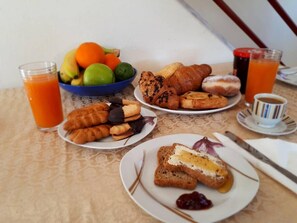 A breakfast table with croissants, pastries, a bowl of fruit, and a glass of orange juice. - Sweet Little Home Trikala (Pyli)