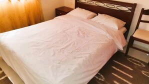 A neatly made bed with a wooden headboard and white bedding. - Sweet Little Home Trikala (Pyli)