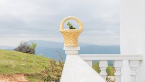 Une balustrade blanche surmontée d’un panier en osier, d’où l’on peut admirer une colline verdoyante et des montagnes lointaines.