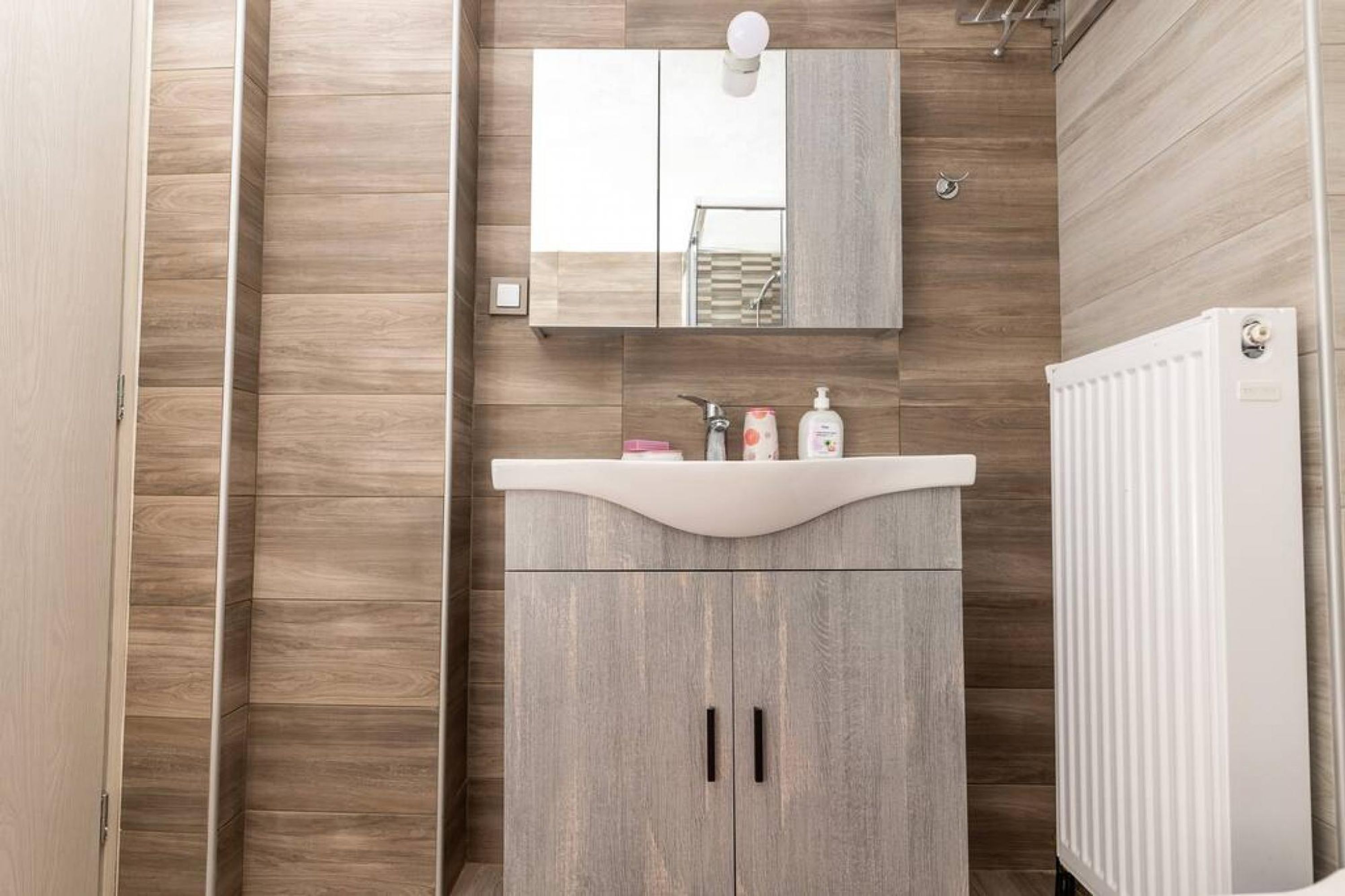 A modern bathroom with a wooden wall, a white sink, and a mirror above it.