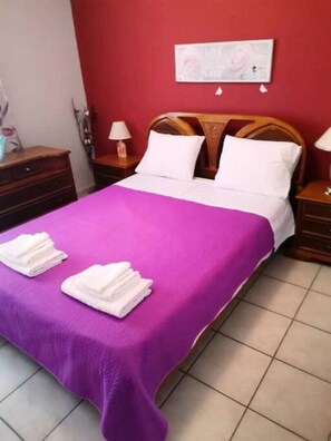 Una habitación de hotel con una cama, una colcha morada, almohadas blancas y dos toallas blancas sobre la cama.